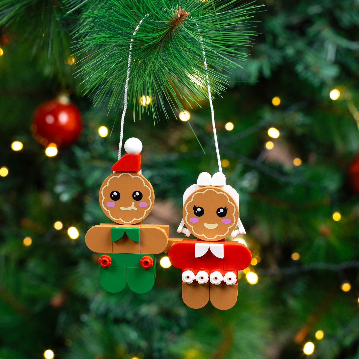 Two gingerbread-themed Christmas ornaments hanging on a tree with lights.