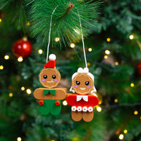 Two gingerbread-themed Christmas ornaments hanging on a tree with lights.