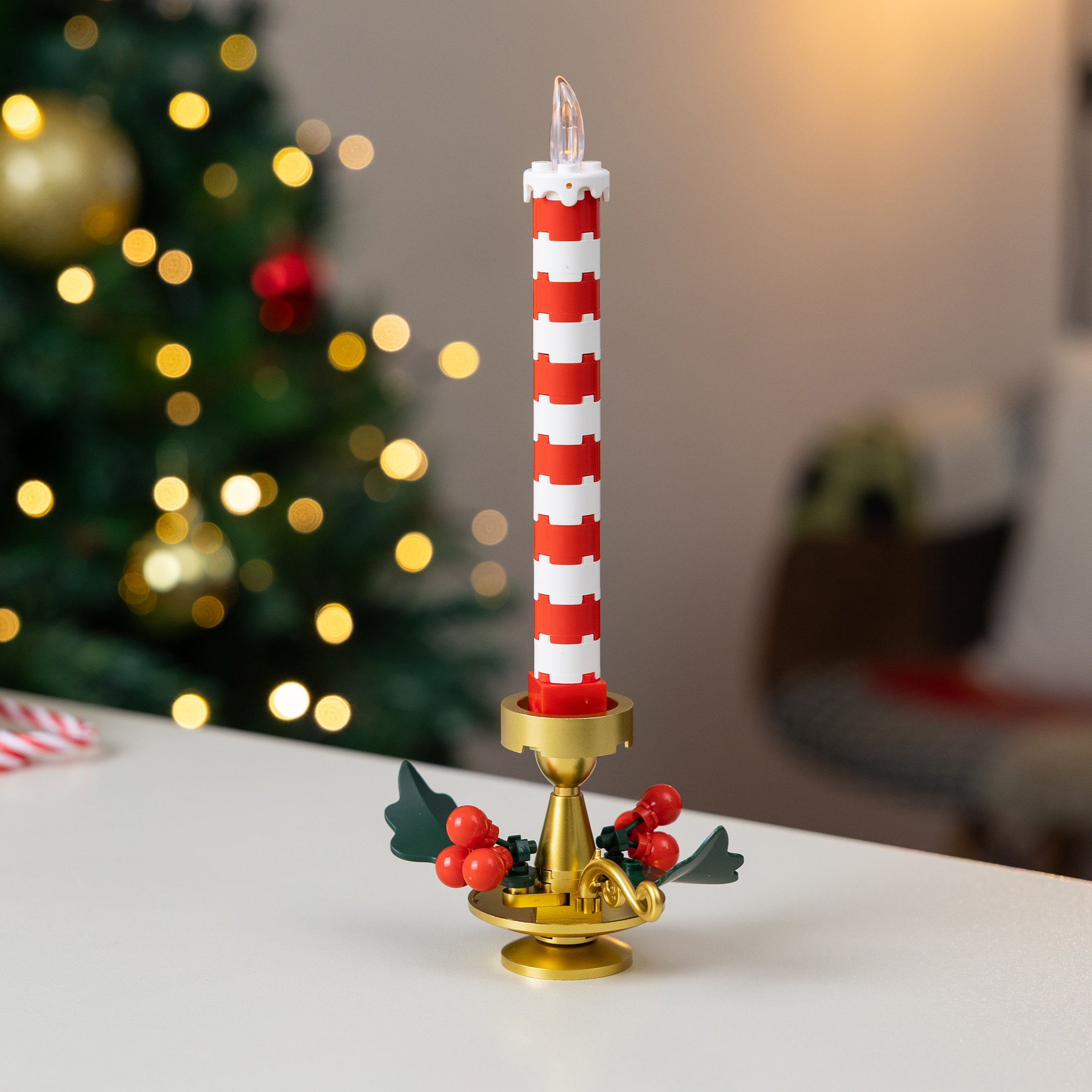 Decorative candle with red and white stripes on a gold holder in front of a Christmas tree.
