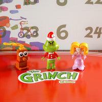 Three toy figures in front of a calendar with 'The Grinch' branding.