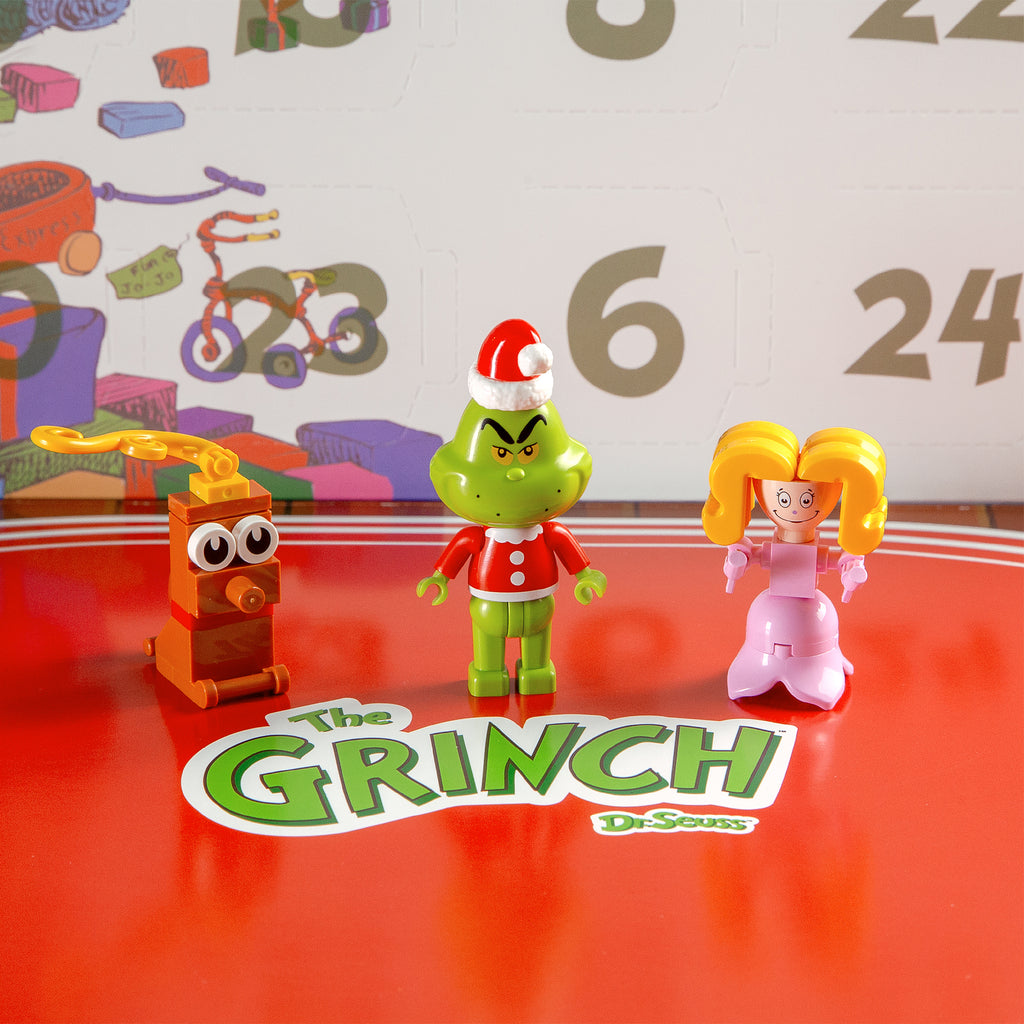 Three toy figures in front of a calendar with 'The Grinch' branding.