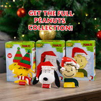 Peanuts-themed figurines with packaging on a wooden surface with a Christmas tree in the background.