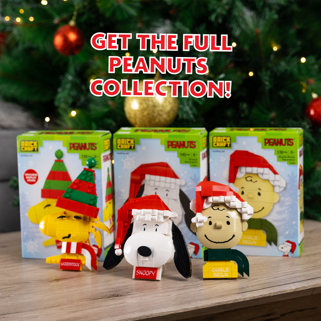 Peanuts-themed figurines with packaging on a wooden surface with a Christmas tree in the background.