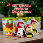 Peanuts-themed figurines with packaging on a wooden surface with a Christmas tree in the background.