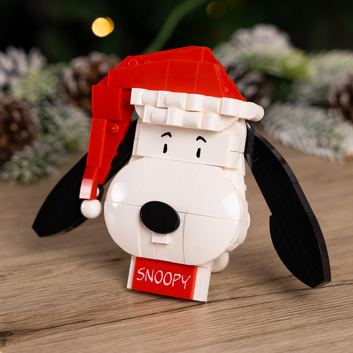 Snoopy figure wearing a Santa hat on a wooden surface with a festive background.