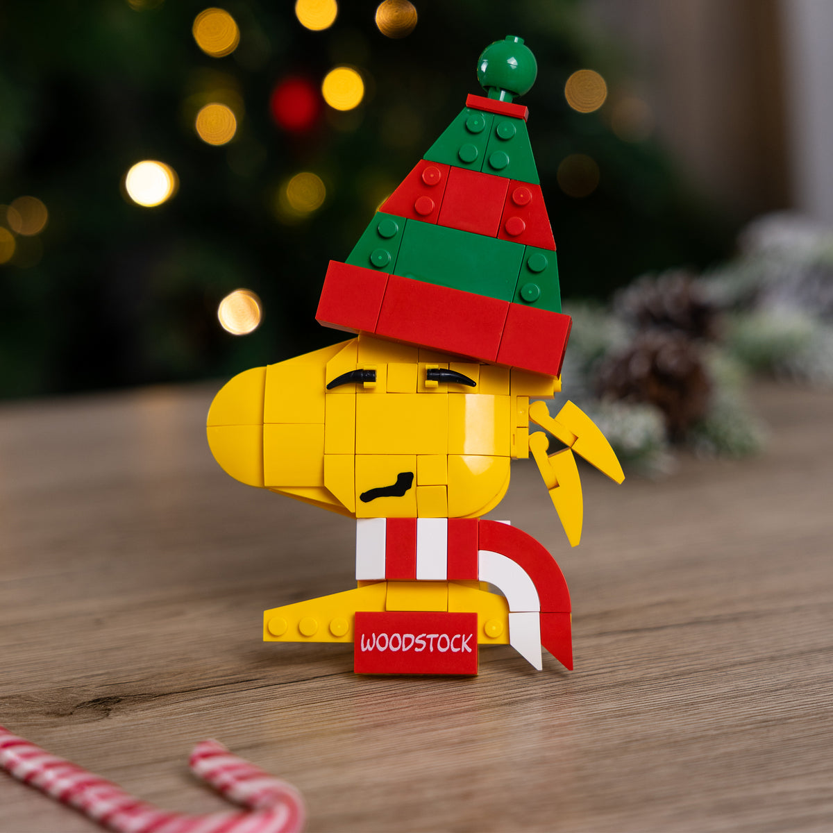 Brick figure of Woodstock with a Christmas hat on a wooden surface with a blurred festive background.
