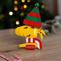 Brick figure of Woodstock with a Christmas hat on a wooden surface with a blurred festive background.