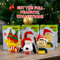 Peanuts-themed figurines with packaging on a wooden surface with Christmas tree in the background.
