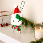 Christmas-themed Hello Kitty ornament with a Santa hat on a table with a candle and greenery.