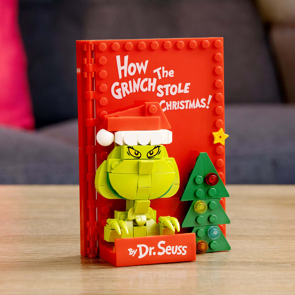 Grinch figure with a red book titled 'How the Grinch Stole Christmas' by Dr. Seuss on a wooden surface.
