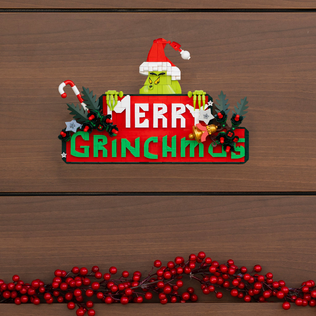 Decorative sign with Grinch face and 'Merry Grinchmas' text on a wooden background.