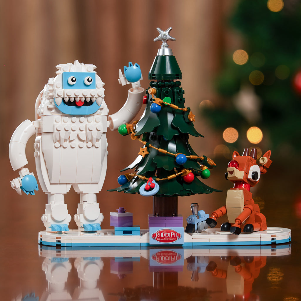 Toy figure of Bumble, a Christmas tree and Rudolph on a reflective surface.