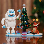 Toy figure of Bumble, a Christmas tree and Rudolph on a reflective surface.