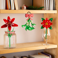Decorative flowers in jars on a wooden shelf with books and a small Christmas tree.