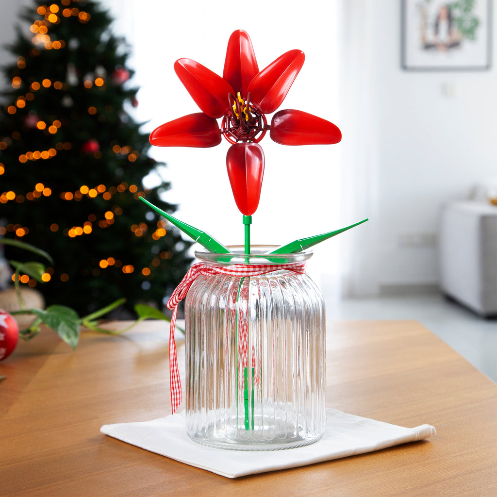 Clear glass jar with a red flower decoration on a wooden table, Christmas tree in the background