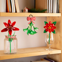 Decorative red and green flowers in glass containers on a wooden shelf.