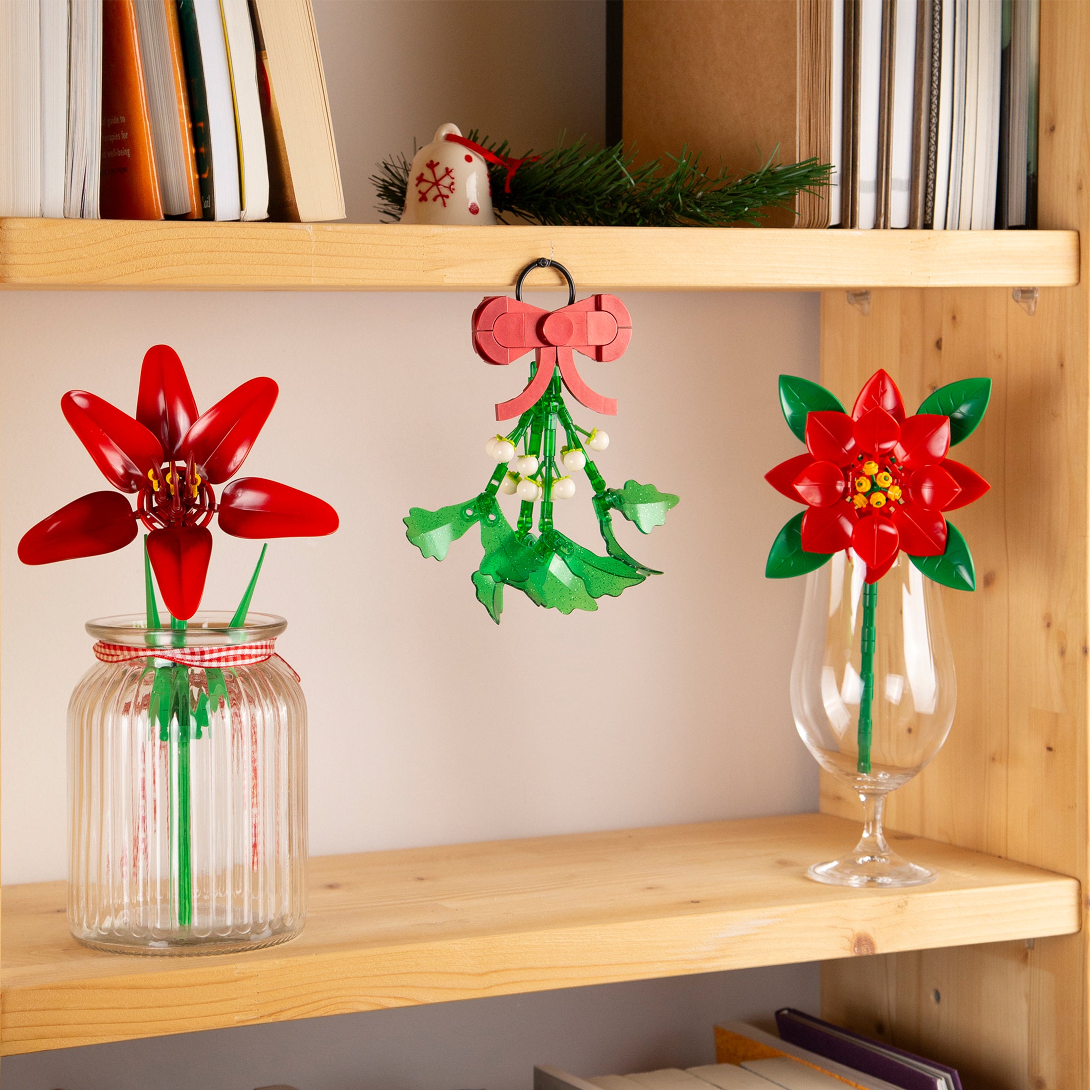 Decorative red and green flowers in glass containers on a wooden shelf.