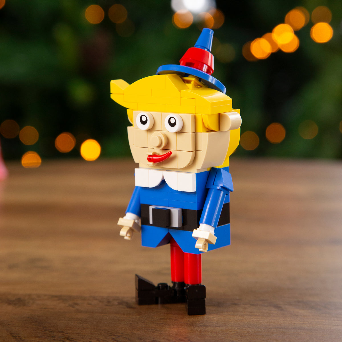 Toy figure of Hermey the Elf with a hat and blue outfit on a wooden surface with blurred lights in the background