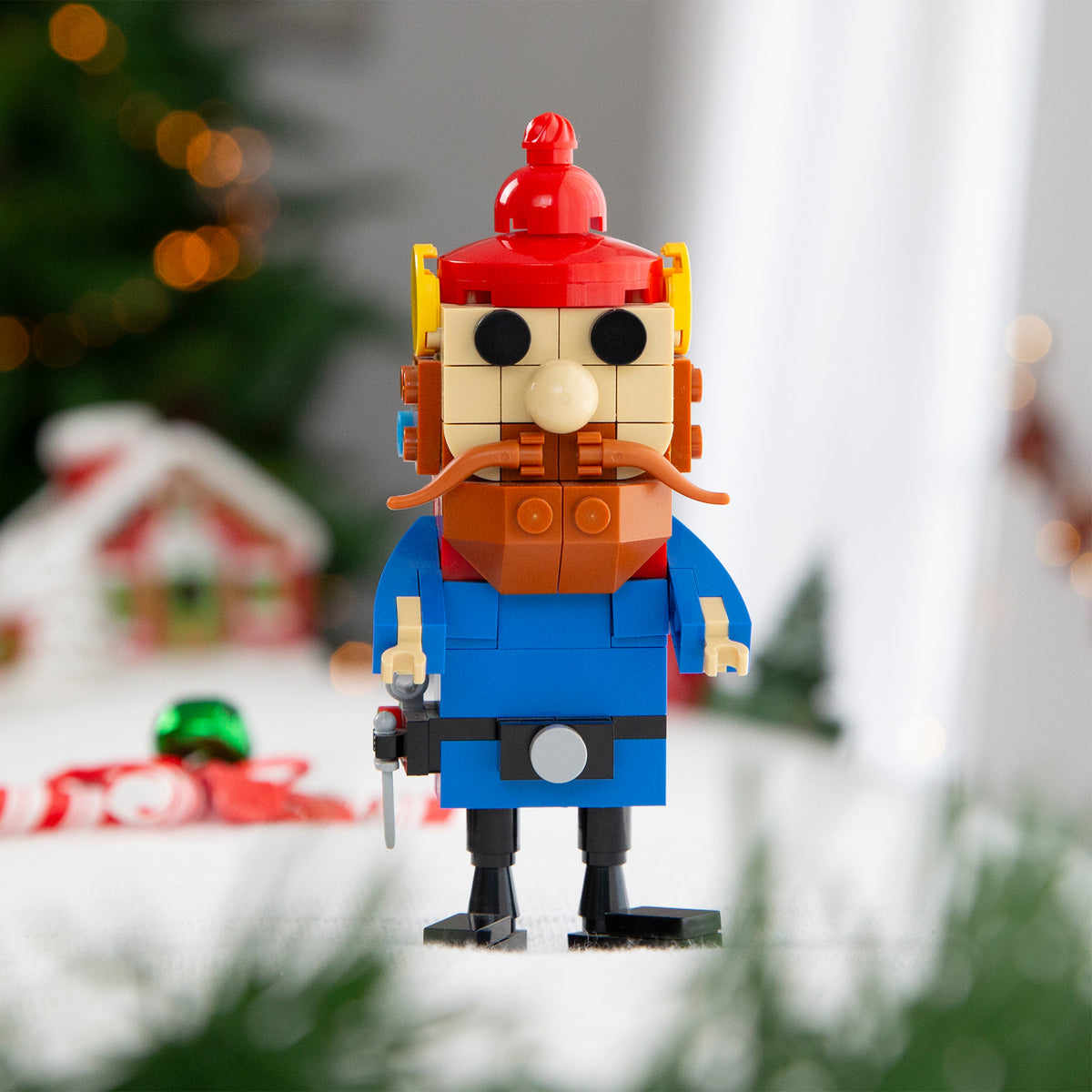Toy figure made of interlocking bricks with a red hat and blue coat, set against a blurred festive background.